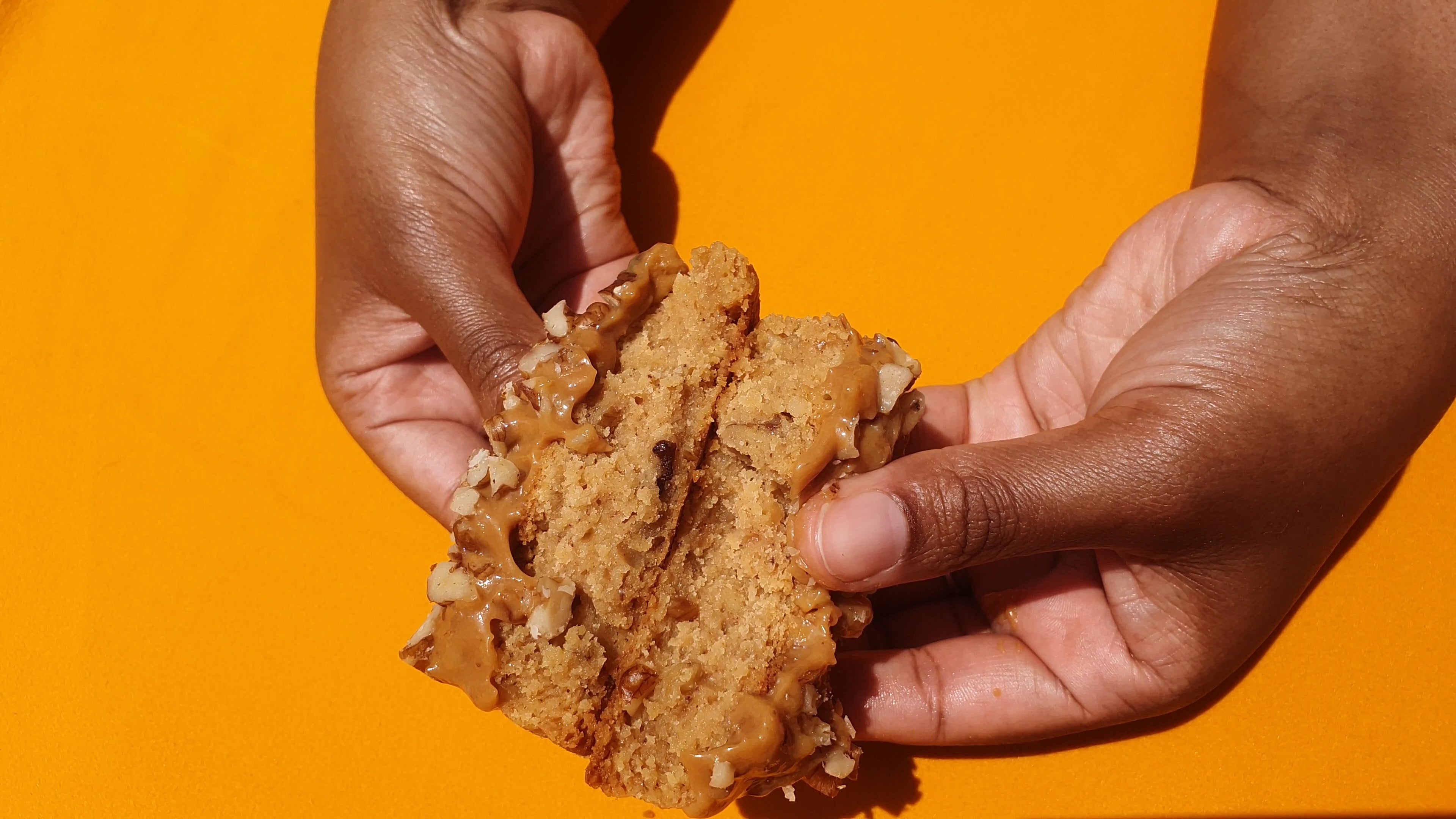 Hands holding a piece of cookie dough against an orange background