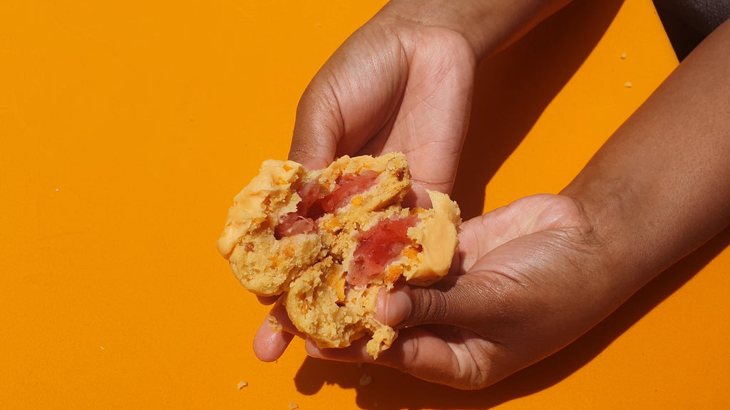 Hand holding a cookie with visible filling against an orange background
