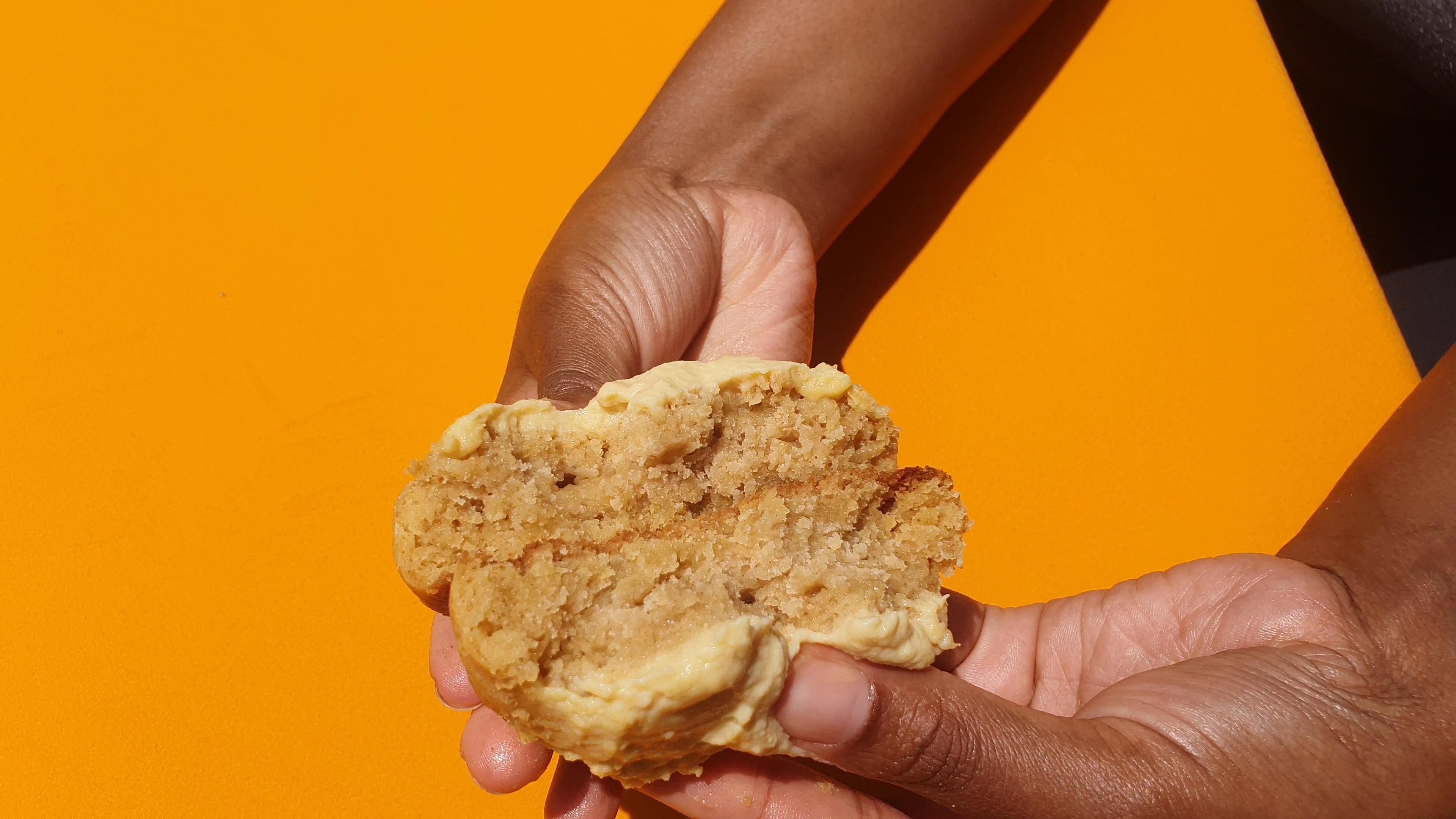 Hand holding a piece of Cookie against an orange background
